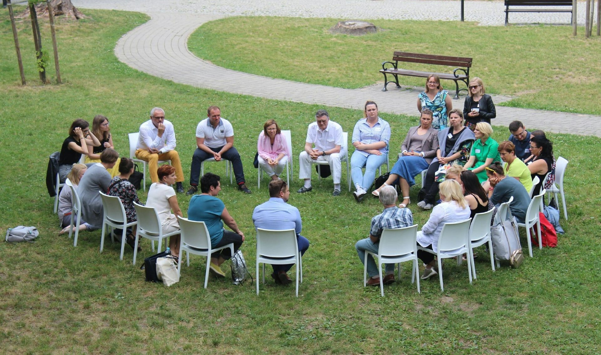 Menschen sitzen im Stuhlkreis auf einer Wiese im Park und sprechen miteinander