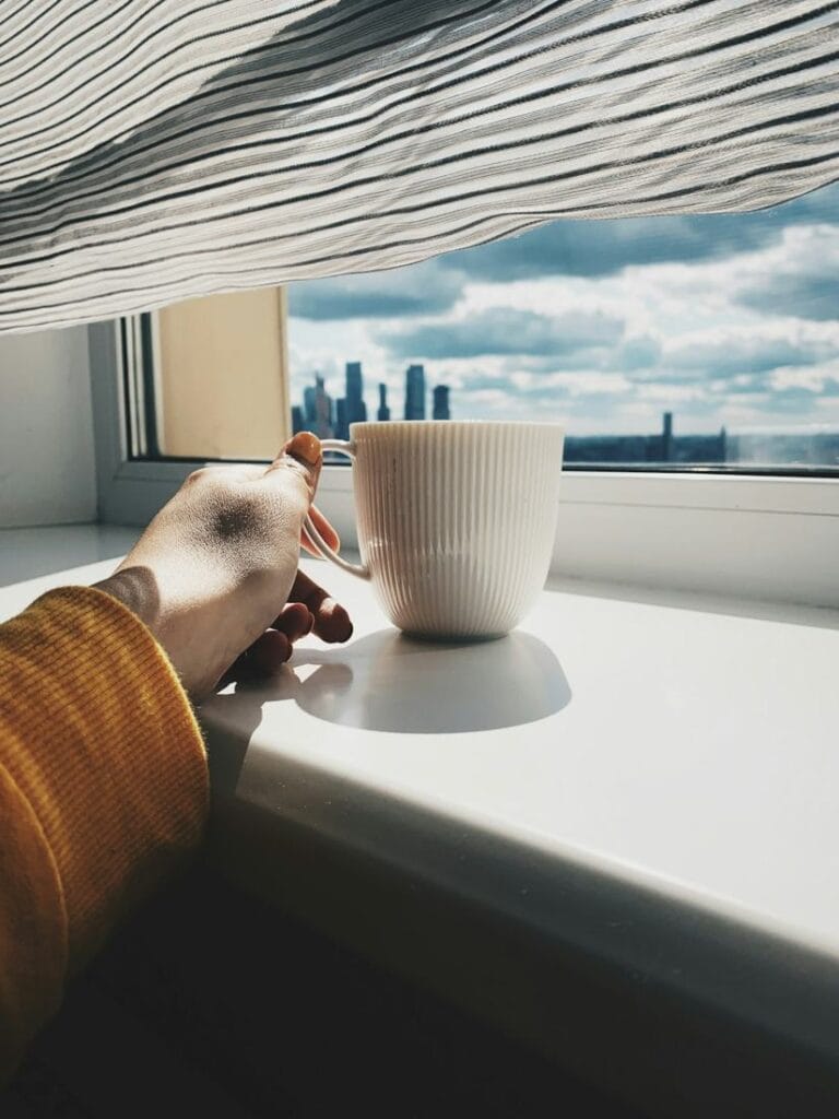 Hand an einer Tasse am Fenster